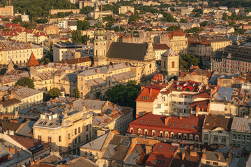 Naklejka premium Golden hour light bathes a historic European cityscape of tiled rooftops, church towers, narrow streets, and layered urban textures below.