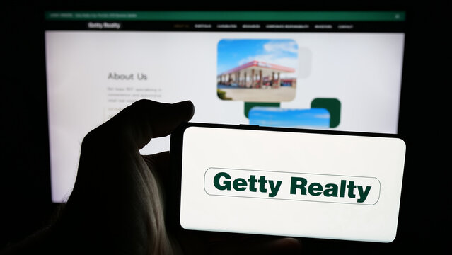 Stuttgart, Germany - 01-15-2026: Person holding mobile phone with logo of US real estate company Getty Realty Corp. on screen in front of web page. Focus on phone display.