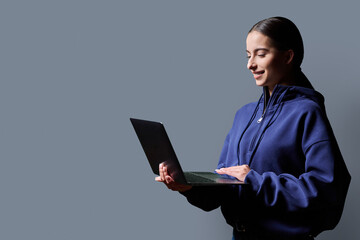 Portrait of smiling teenage girl holding laptop on gray studio background