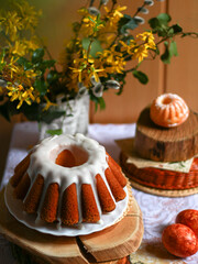 Traditional Easter cake on wooden stands with spring flowers on festive table. Concept of Easter celebration, food styling background for banner, card, retail marketing.