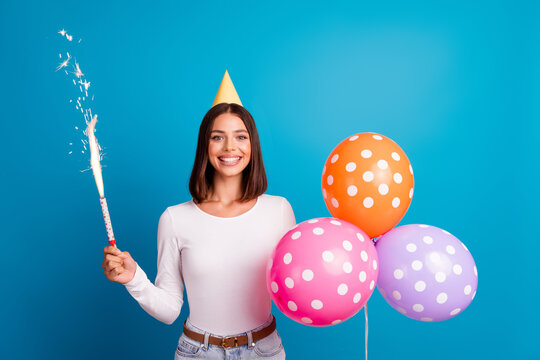 Young woman celebrates birthday with balloons and sparkler on a bright blue background
