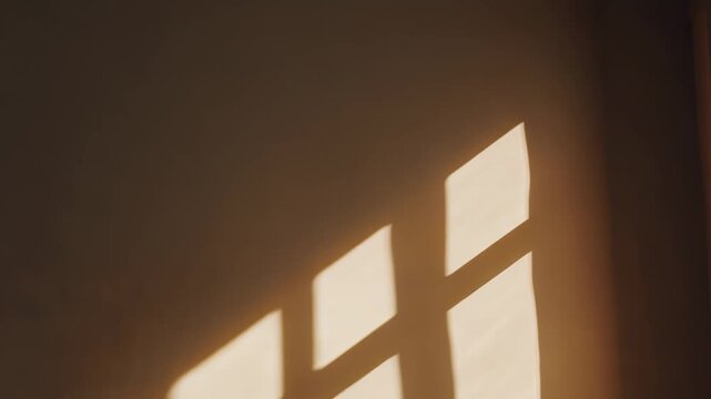 Warm sunlight streaming through a window creating a geometric grid shadow pattern on a beige wall, evoking a serene and minimalist interior atmosphere