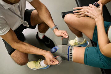 Obraz premium Caucasian young adult woman receiving knee support adjustment from male physical therapist during rehabilitation session, therapist securing orthopedic brace on patients leg