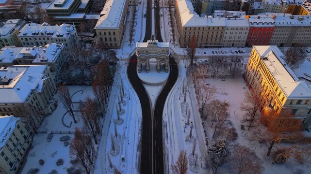Cinematic aerial of Siegestor Victory Gate in Munich Germany. Neoclassical Triumphal Arch Triumphbogen and Friedensmahnmal Peace Memorial at Ludwigstrasse under winter snow with historic lions