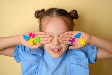 Smiling child covering eyes with colorful puzzle pieces and hearts. Autism awareness and inclusion...