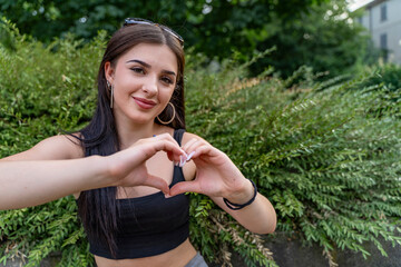 Young woman smiling, showing love gesture with hands in a park