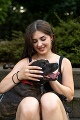 Young woman petting a happy pitbull dog sitting outdoors feeling friendship and connection
