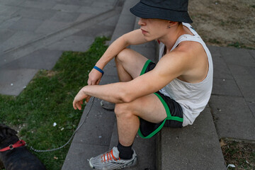 Young man wearing a bucket hat and tank top, sitting on steps with his dog on a leash