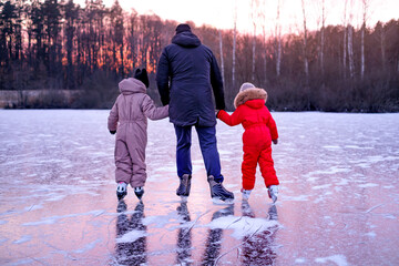 Father holding hands with two children while skating on frozen lake at winter sunset. Family...