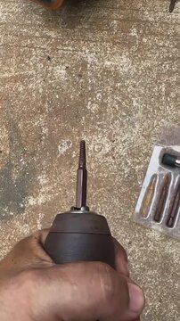 Hand holding cordless drill with screw extractor bit for removing stripped damaged screws on workshop bench with metal extraction set and hardware tools diy home repair and maintenance concept