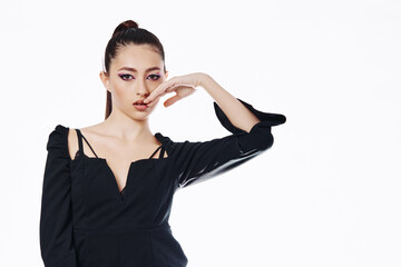 Young woman with sleek hairstyle and creative black outfit poses with fingers near face. Studio...