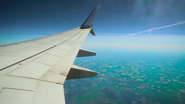 Passenger airplane flying under chemtrail over patchwork fields. Jet cruising beneath white trail across farmland mosaic. Aircraft gliding below vapor line above agricultural landscape