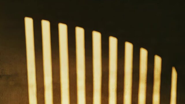 Warm sunlight streams through a window, casting strong, parallel striped shadows across a textured concrete wall and extending onto the empty floor, creating an abstract pattern