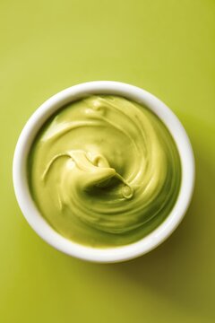 Pistachio cream spread in a white bowl on a green background. Green color. Top view
