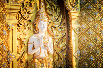 Extreme close-up view of the serene face of a traditional Thai Buddhist Deva (Angel) relief sculpture with intricate golden details. The image captures the artistic craftsmanship at Wat Chan Tawan Tok