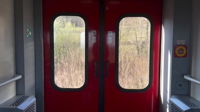 Red train doors with grassy view from inside the carriage  