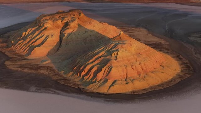 Aerial view of a majestic mountain casting long shadows across the arid, textured landscape, contrasting the light and dark tones, Karynzharyk, Mangystau Region, Kazakhstan.