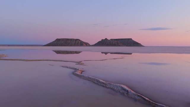 Aerial view of the serene desert landscape reflecting rock formations in shallow pools beneath a pastel sky, Karynzharyk, Mangystau Region, Kazakhstan.
