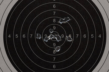 Close up of a black paper shooting target with multiple bullet holes in the center bullseye from...