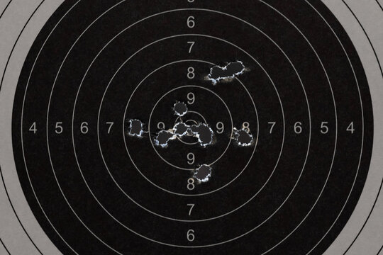 Close up of a black paper shooting target with multiple bullet holes in the center bullseye from gun range practice.