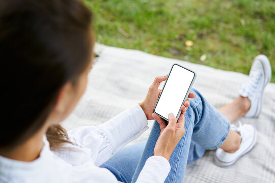 Phone mock-up. Woman using smartphone with blank empty screen sitting on blanket outdoors