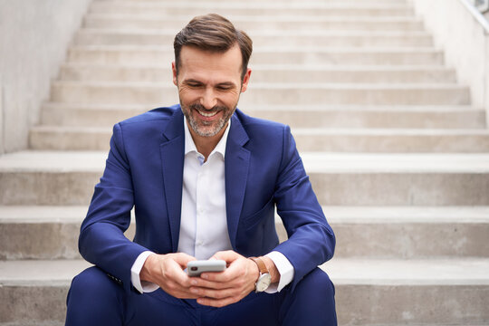 Portrait of smiling businessman sitting on stairs using mobile phone
