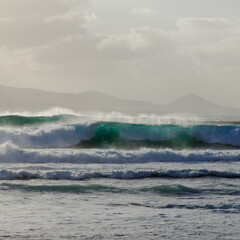 Fototapeta premium Gran Canaria, view towards Atlantic ocean from El Confital beach on the edge of Las Palmas de Gran Canaria, big waves crushing, rain in the mountains 