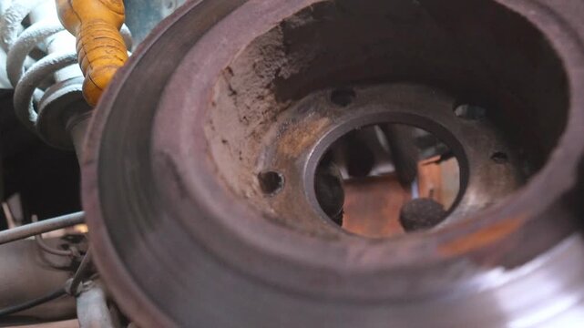 A gloved professional mechanic carefully removes a worn and rusted car brake disc from the hub while servicing or repairing the car in a car repair shop or garage