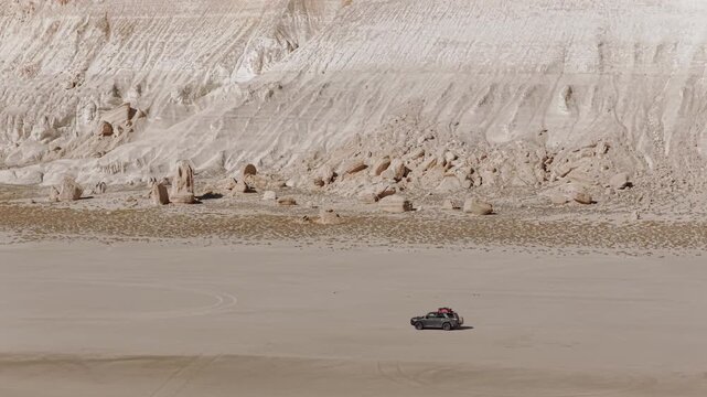 Aerial view of a car parked on the expansive Tuzbair Sor, contrasted against the stark white cliffs, Tuzbair, Mangystau Region, Kazakhstan.