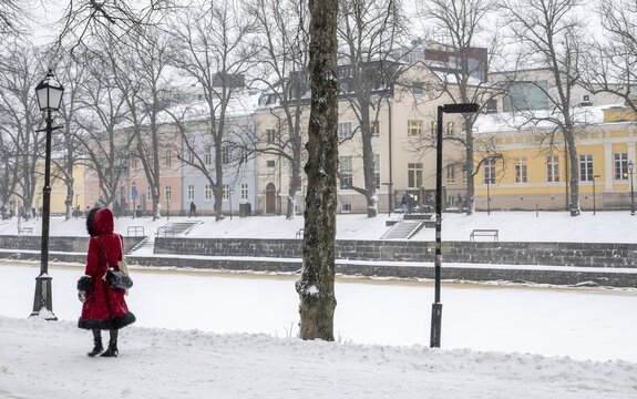 Woman in red winter coat walks along the frozen Aurajoki river, wintery Turku or Swedish &Aring;bo, Varsinais-Suomi, Finland
