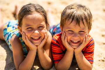 Two children smiling while lying on sand at beach in summer  