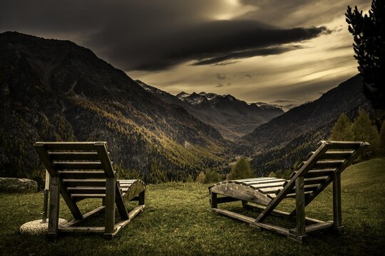 Deck chairs on a mountain meadow with autumnal mountain forest and threatening cloudy sky, Martell Valley, Merano, Vinschgau, South Tyrol, Italy
