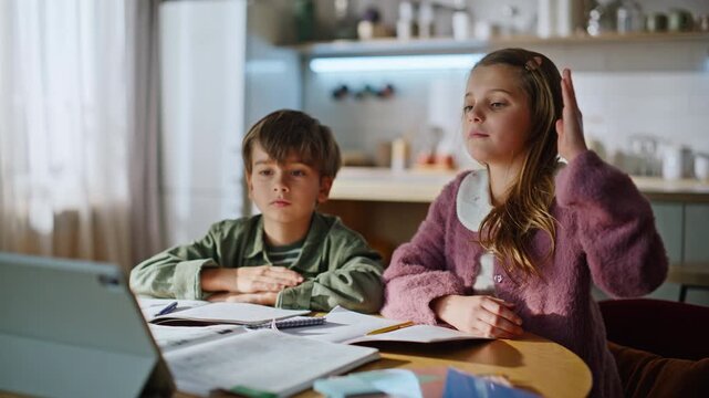 Brother sister studying online remote at home closeup. Schoolgirl raising hand