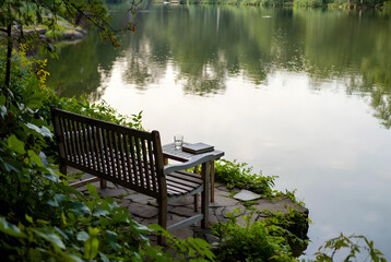 Fototapeta premium Wooden Garden Bench with Book and Glass of Water by Calm Lake