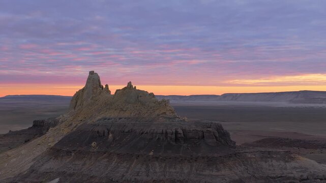 Aerial view of a rugged mountain under a sky painted with soft pastel hues of dawn, casting long shadows over the arid landscape, Shetpe, Mangystau Region, Kazakhstan.