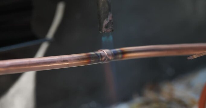 A technician or worker is soldering copper pipes; an air conditioning technician.