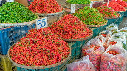 Fototapeta premium Thailand vegetable market, Market stands display piles of red and green chili peppers for sale in a busy area during the day