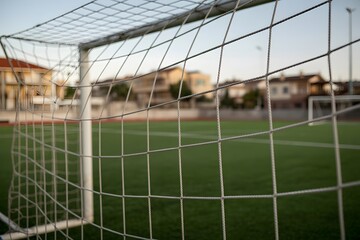 Empty soccer goal net view looking out onto green football pitch during peaceful afternoon