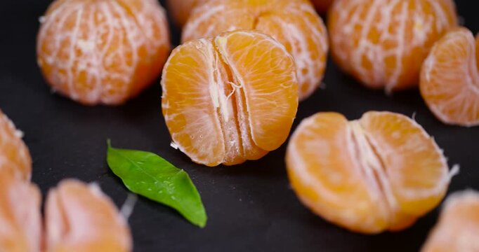 sliced juicy peeled orange tangerine on a black slate table, orange small mandarin without peel on a black slate board, tangerine divided into small slices