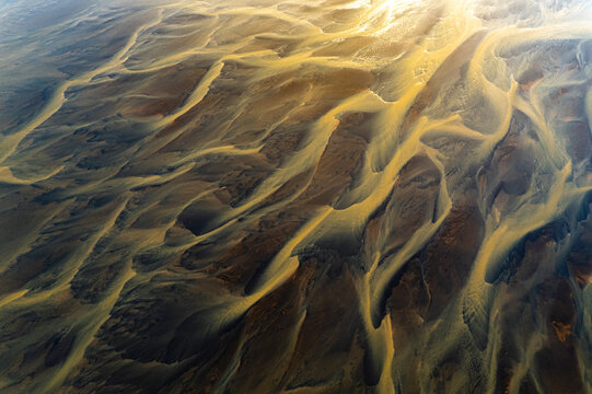Aerial view of braided river channels carve paths through the landscape, a symphony of ochre and dark earth tones creating a mesmerizing pattern, Selfoss, Southern Region, Iceland.