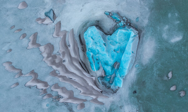 Aerial view of a heart-shaped turquoise glacier surrounded by swirling icy water, creating a striking contrast of color and texture, Selfoss, Southern Region, Iceland.