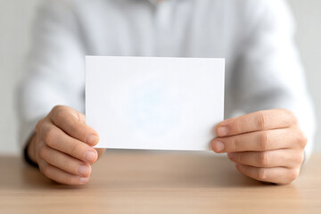 A person is holding a blank white card in front of them, resting on a wooden surface, creating a minimalistic and neutral aesthetic.
