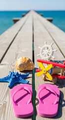 Fototapeta premium Wooden dock view with sea elements: seashell, starfish, toy airplane, ship wheel, flip flops. Represents summer vacation, nautical theme and travel concept