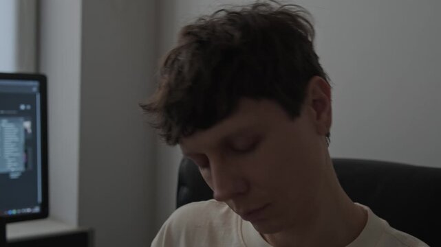 Young man doing neck exercise on office chair in home office during work break, remote freelancer stretching at computer, healthy lifestyle and sedentary job prevention