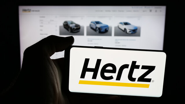 Stuttgart, Germany - 01-19-2026: Person holding mobile phone with logo of car rental company Hertz Global Holdings Inc. on screen in front of web page. Focus on phone display.