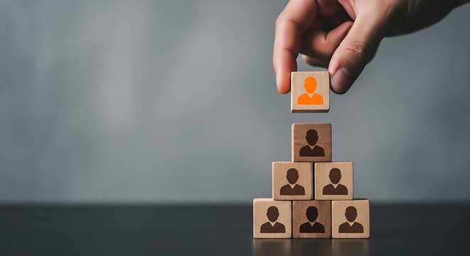 Hand carefully placing the final wooden block representing a key employee onto the top of a growing human resources organizational pyramid structure