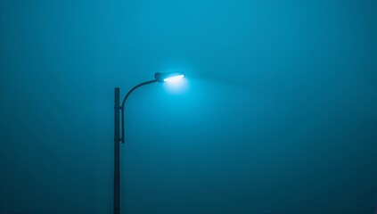 Emitting street lamp at roadway, metal pole curved arm casting blue halo through fog, copy space