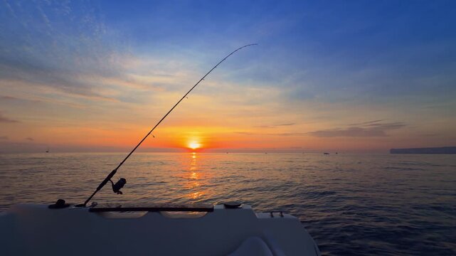 Offshore bottom fishing at sunset from boat with rod over calm sea