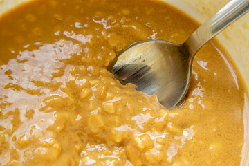 Closeup shows spoon in thick creamy paste inside bowl. Smooth and chunky texture visible on surface.