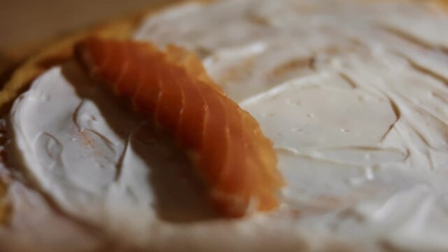 Laying salmon slices as filling on yellow pancake anointed with creamy cheese, macro view